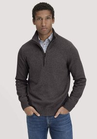 Dunkelgrauer Reißverschluss-Pullover aus weichem Strickmaterial, mit gerippten Bündchen und Saum, getragen über einem weißen mit Blumenmuster.