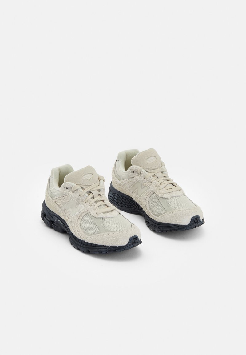 Paire de baskets de sport beige et noire avec semelles texturées, empiècements en maille et fermeture à lacets sur fond blanc.