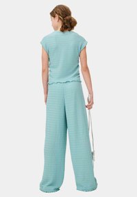 Lichtblauwe twee-delige outfit van textuurstof. Top met kapmouwen en een gerimpelde zoom; wijde broek met een losse pasvorm.