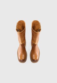 Botas de cuero marrón hasta la rodilla con un acabado suave, que presentan una parte superior ligeramente elevada, detalles de costura y tiradores a los lados.