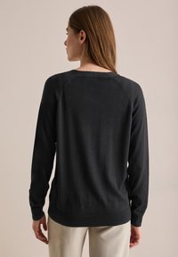 Pull noir à manches longues avec col rond et poignets côtelés. Présente une texture lisse et un design épuré. La vue arrière montre une coupe décontractée.