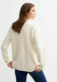 Maglione a coste color crema con maniche lunghe, motivo testurizzato e polsini a coste. Indossato con jeans scuri, visto da dietro.