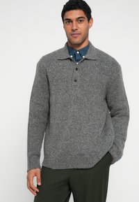 Γκρι πλεκτό πουλόβερ με γιακά, τέσσερα κουμπιά και άνετη εφαρμογή, υφή υφάσματος, συνδυασμένο με μπλε πουκάμισο με κουμπιά από κάτω.