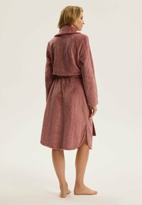 Długa różowa szata z fakturowanym wzorem warkoczowym, z długimi rękawami, paskiem w talii oraz długością do kolan z bocznymi rozporkami.