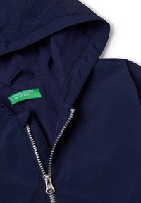Navy blue hooded jacket with a silver zipper, featuring a green "United Colors of Benetton" label inside the collar. Smooth texture.