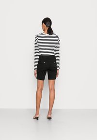 Zwarte denim shorts en een zwart-wit gestreept overhemd met lange mouwen. Het overhemd heeft een ronde halslijn en aansluitende mouwen.