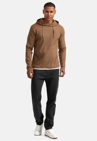 Felpa a maniche lunghe marrone a coste con cappuccio regolabile, abbinata a jeans scuri e sneakers bianche. Design semplice con una vestibilità comoda.