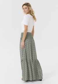 Zelena maxi krila s cvetnim vzorcem, ki ima nabran pas in večplastno zasnovo. V kombinaciji z belim topom s kratkimi rokavi.