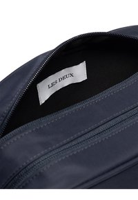 Námorná modrá taška s hladkým povrchom, so zipsom a označením "LES DEUX" vo vnútri. Vybavená kontrastným prešívaním a dvoma priehradkami.