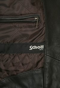Musta nahkatakki, jonka sisällä on ruskea tikattu vuori, vetoketjullinen tasku ja musta nauha, jossa on "Schott N.Y.C." -logo.