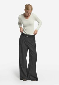 Ribbad vit långärmad topp i kombination med högmidjade mörkgrå vida byxor och ett svart bälte med en silverfärgad spänne.