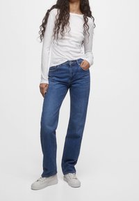 Camiseta blanca de mangas largas y jeans rectos azules. El material parece ser algodón. Los jeans presentan un diseño clásico de cinco bolsillos y un ajuste relajado.