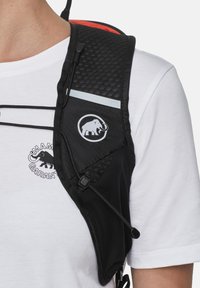 Zwarte hydratatievest met mesh-textuur, voorzien van een reflecterende strip, logopatch en verstelbare bandjes. Draagt over een wit shirt.