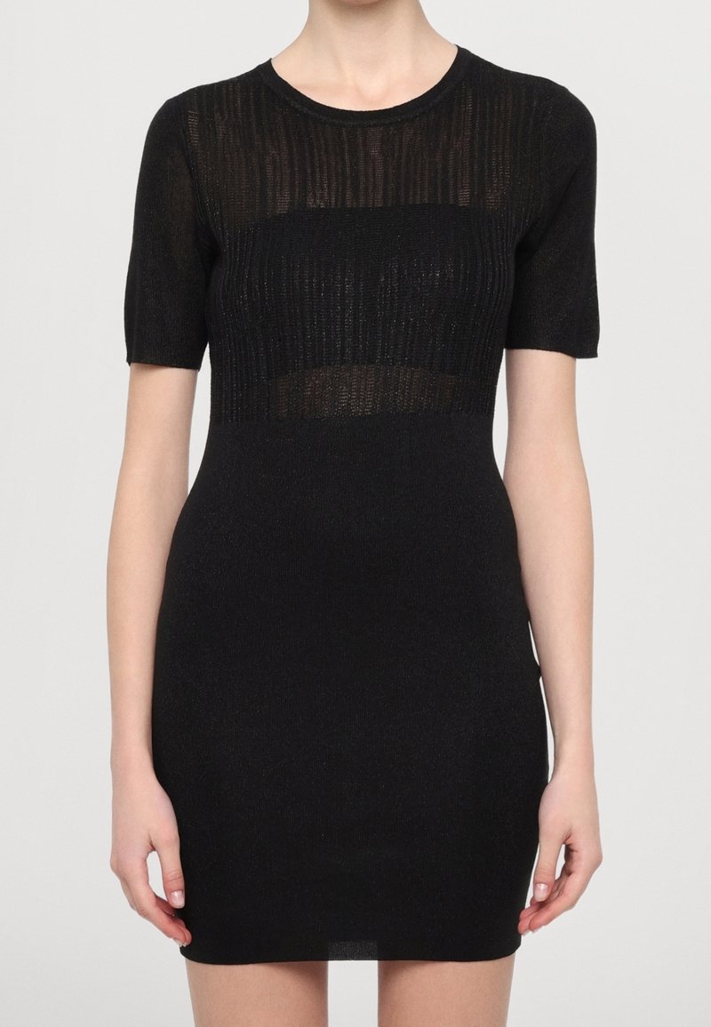 Personne portant une robe noire ajustée à manches courtes avec un motif en maille côtelée transparente sur le haut de la poitrine et les manches.