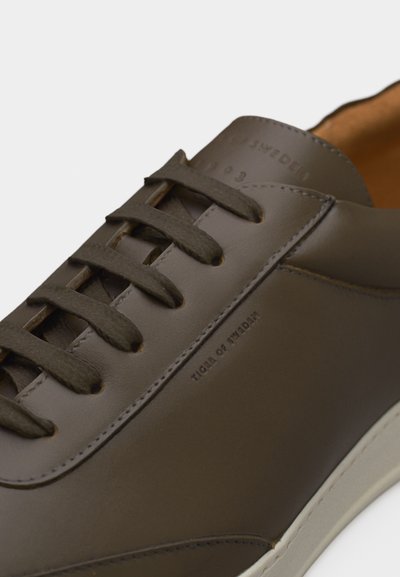 Brązowy skórzany sneaker na sznurowadła z wytłoczonym napisem „TIGER OF SWEDEN” po boku i na języku, z białą podeszwą i gładkim wykończeniem.