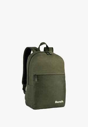 Sac à dos en tissu vert olive avec une surface lisse, poche avant zippée, bretelles renforcées et un panneau de texture hexagonale subtile.