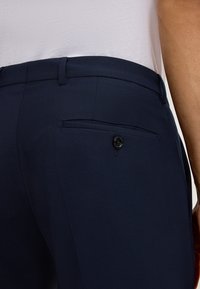 Marineblaues Dresshose zeichnet sich durch eine elegante Textur und eine maßgeschneiderte Passform aus. Sie verfügt über eine geknöpfte Gesäßtasche und Gürtelschlaufen. Der Bund ist gerade geschnitten.