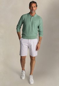 Muntgroene polo met lange mouwen en geribbelde kraag, gecombineerd met witte shorts met streepjes en witte sneakers.