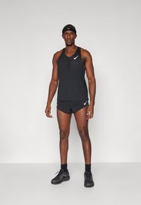 Svart trenings tank topp og shorts i pustende stoff, med mesh detaljer og hvit Nike-logo. Modell iført svarte sko og hodebånd.