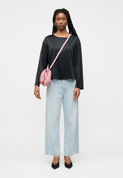 Γυναίκα με μακριά κοτσίδα, που φοράει μαύρο μπλουζάκι με μακριά μανίκια, ανοιχτόχρωμο τζιν παντελόνι με φαρδιά μπατζάκια, μαύρα τακούνια και ροζ καπιτονέ τσάντα χιαστί.