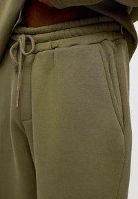 Olijfgroene joggingsbroek van een zachte katoenmengsel, met een elastische tailleband met een trekkoord en zijzakken. Glad textuur.