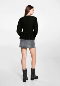 Black, long-sleeve blouse with a peplum waist; paired with a grey denim skirt and knee-high black boots, showcasing a casual outfit.