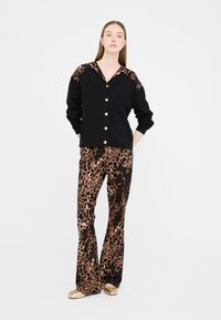 Top nero con dettagli in stampa leopardata, bottoni dorati; abbinato a pantaloni marroni con stampa leopardata e gamba svasata. Tessuto liscio, design aderente.