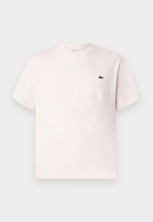 T-shirt à col rond rose clair à manches courtes avec une poche poitrine arborant un petit logo de crocodile vert.