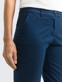 Marineblauwe broek met een gladde textuur, voorzien van een knoopsluiting, zijzakken en een subtiele glans; gesneden pasvorm rond de taille en heupen.