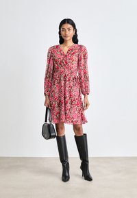 Pink floral wrap dress with long sleeves and a flared skirt, paired with knee-high black boots and a small black handbag.