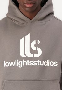 Gray hoodie featuring a large white logo with "lows" and "studios" text, soft material, kangaroo pocket, and drawstring hood.