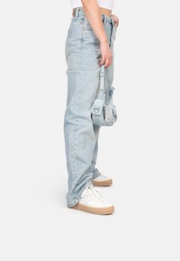 Hellblaue, hoch geschnittene Jeans mit lockerer Passform, kombiniert mit weißen Sneakern und einer kleinen hellblauen Tasche. Glatte Denim-Textur.