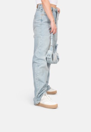 Jeans taille haute bleu clair avec une coupe ample, associés à des baskets blanches et un petit sac bleu clair. Texture denim lisse.