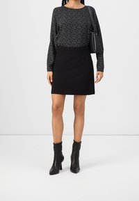 Svart långärmad topp med vitt prickmönster, tillsammans med en svart minikjol. Bärs med svarta klackboots. Enkelt, stilrent design.