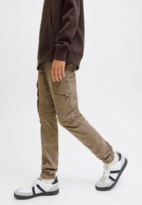 Spodnie cargo w kolorze khaki z wieloma kieszeniami, zwężanymi mankietami i gładką tkaniną z mieszanki bawełny. Połączone z białymi trampkami z czarnymi akcentami.