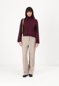 Burgundi turtleneck megztinis, trumpas kirpimas, derinamas su bežinėmis aukšto juosmens kelnėmis. Šltas, tiesus dizainas su priekinių kišenių. Juodi batai.