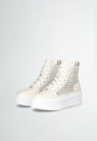 Hoge sneakers met een romig witte synthetische bovenkant en gaas zijpanelen, dikke witte platformzool en een gouden logo op de zijkant.