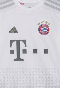 Camiseta de fútbol blanca de adidas con el escudo del FC Bayern München, el logo del patrocinador en gris y un sutil patrón geométrico en la parte inferior.