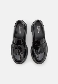 Mocassins en cuir noir verni avec une finition brillante, présentant un accent de gland surélevé et des coutures détaillées sur le devant. Semelles épaisses et texturées.
