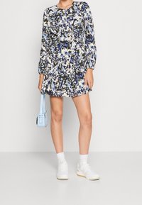 Sininen ja valkoinen kuvioitu mini mekko, jossa on pitkät hihat ja röyhelöhelma. Yhdistetty vaaleansiniseen käsilaukkuun ja Valkoisiin tennareihin.