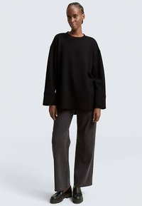 Felpa nera oversize con spalle scese, polsini a coste e orlo dritto, abbinata a jeans grigio scuro a gamba larga e scarpe nere.