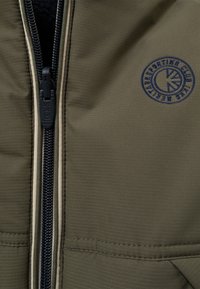 Olijfgroene zip-up jas met marineblauwe accenten, met een opvallende logopatch en een getextureerde stof met een zachte afwerking. Ritssluiting is zichtbaar.