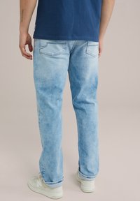 Jeans azzurri chiari con un lavaggio sbiadito, design a cinque tasche e dettagli cuciti. Abbinati a sneakers bianche, con focus sulla vista posteriore.