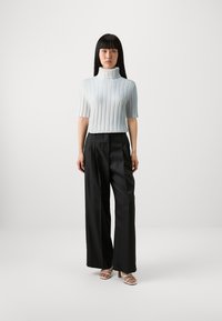 Hellblau gestreifter Kurzarm-Turtleneck-Pullover kombiniert mit schwarzen, plissierten, weit geschnittenen Hosen und beigen Riemchen-Absätzen.
