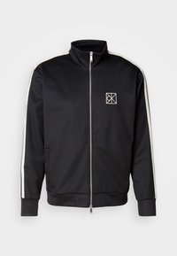 Zwarte zip-up jas met een hoge kraag, voorzien van witte zijstrepen en een klein logo op de borst, gemaakt van een soepel, flexibel materiaal.