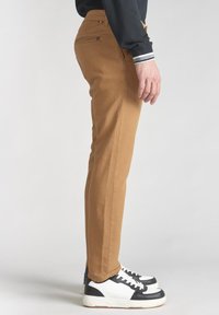 Smalle, camel-kleurige broek van duurzame stof; zijzak met subtiele branding; gecombineerd met zwart-witte sport sneakers.