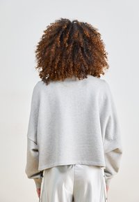 Jasnoszara, oversize'owa bluza z szerokim dekoltem i opuszczonymi ramionami, wykonana z miękkiego materiału. Połączona z błyszczącymi srebrnymi spodniami.