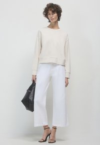 Sweatshirt crema oversize, jeans bianchi a gamba larga, tacchi a strappo neri e una borsa nera. Texture lisce, vestibilità rilassata, design moderno.