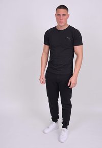 Černé přiléhavé tričko s krátkým rukávem, černé tepláky a bílé tenisky. Jednoduchý design, hladká textura a minimální branding.