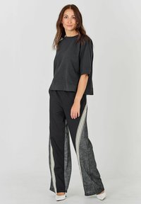 Tricou scurt negru cu mâneci scurte, asortat cu pantaloni lărgi, având secțiuni negre și gri texturat, cu dungi albe pe lateral.